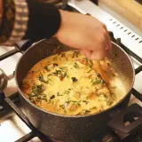 Ręka miesza kremowe curry z zielonymi warzywami w garnku. Idealny garam masala przepis na aromatyczne danie.