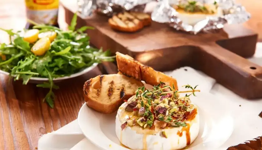 Pyszny camembert z grilla, polany miodem i posypany pistacjami, podany z grzankami i sałatką.