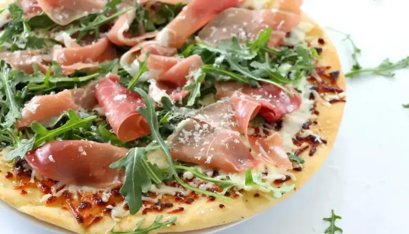 Pyszna pizza prosciutto z rukolą i parmezanem, idealna na letni wieczór.