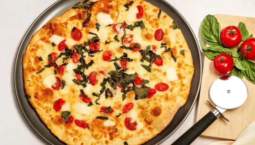 Pyszna pizza z serka wiejskiego, pomidorkami koktajlowymi i bazylią. Idealna na szybki obiad.