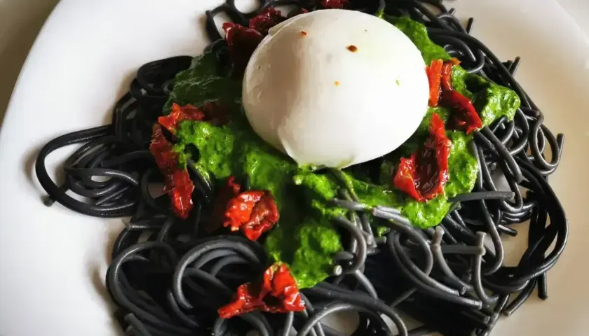 Czarny makaron z zielonym pesto, suszonymi pomidorami i kulką mozzarelli. Wygląda apetycznie!