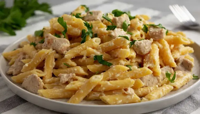 Penne z kurczakiem w kremowym sosie mascarpone, posypane świeżą natką pietruszki. Pyszne danie gotowe do podania.
