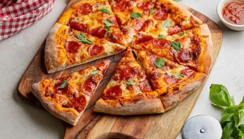 Apetyczna pizza pepperoni z ciągnącym serem i świeżą bazylią, gotowa do podania na drewnianej desce.