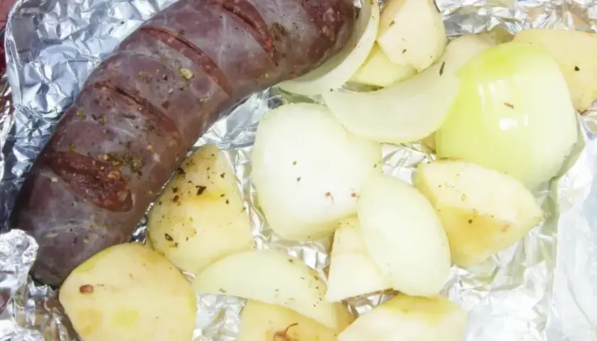 Kaszanka z grilla z cebulą w folii aluminiowej, gotowa do pieczenia. Aromatyczne dodatki podkreślą smak.