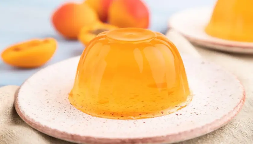 Pomarańczowa galaretka na talerzyku, obok przekrojonych brzoskwiń.