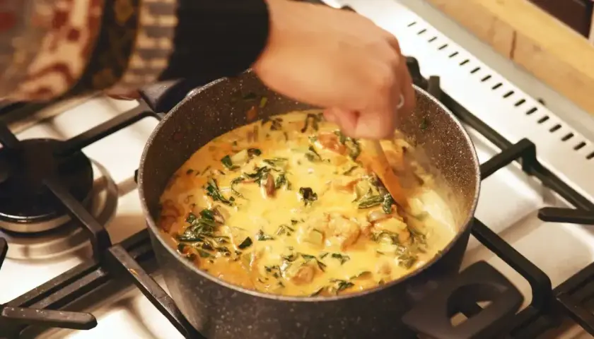 Ręka miesza kremowe curry z zielonymi warzywami w garnku. Idealny garam masala przepis na aromatyczne danie.