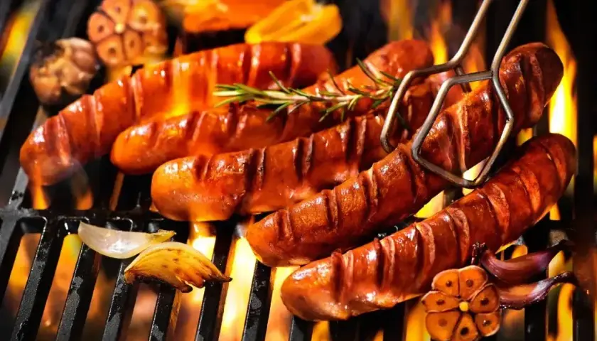 Aromatyczna kiełbasa z grilla skwierczy na ruszcie, otoczona płomieniami i przypieczonym czosnkiem.