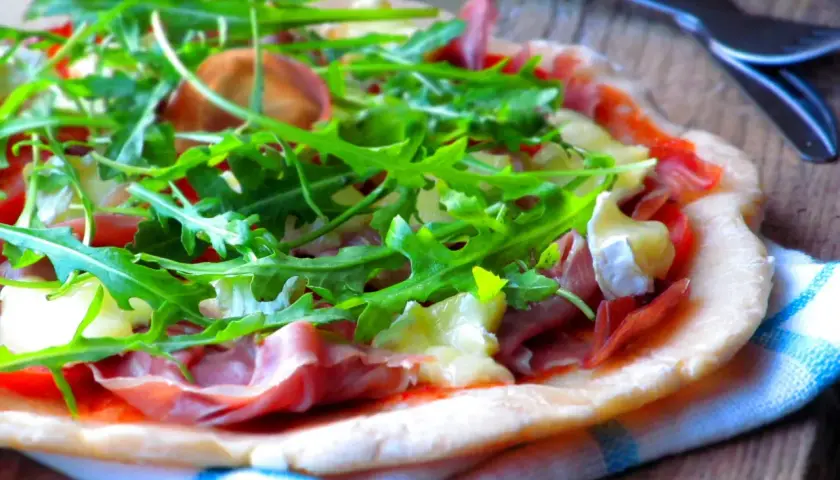 Pyszna pizza parma z rukolą i serem na drewnianym blacie.